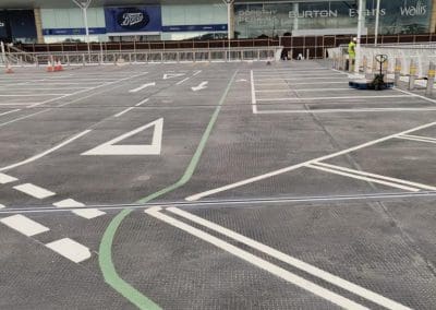 Freshly painted car park lining with white directional arrows, green pedestrian walkway markings, and parking bays at a shopping centre, completed by Bournemouth White Lining for professional car park lining services