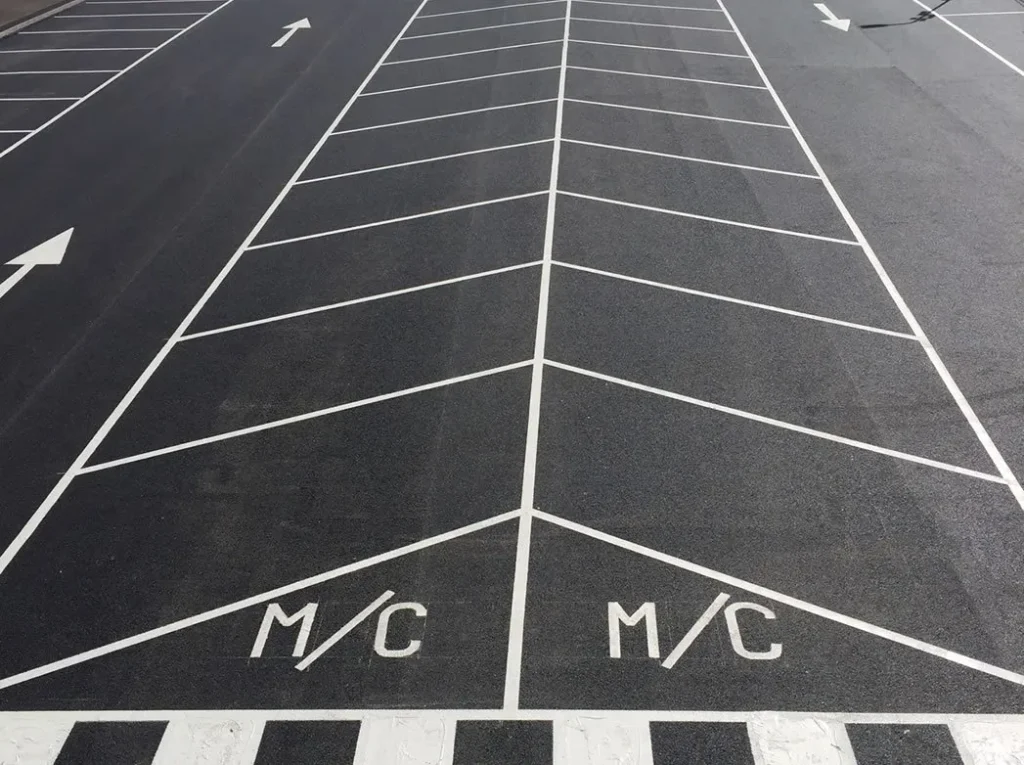 Close-up of freshly painted car park lining in Dorset, featuring clear white directional arrows and dedicated motorcycle parking bays.